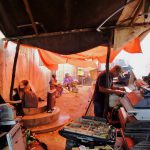Zanzibar, Tanzanie. Mars 2018. Des hommes réparent des appareils électroniques usagés importés, tandis que les femmes préparent la nourriture en arrière-plan. Copyright BAN.